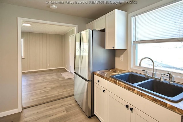 kitchen featuring a sink, white cabinetry, freestanding refrigerator, light wood finished floors, and baseboards