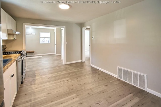 kitchen featuring gas range, light wood-style flooring, visible vents, and white cabinets