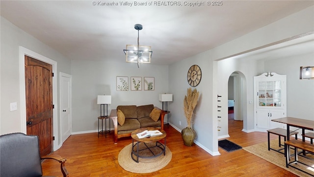 living area featuring arched walkways, light wood-style flooring, an inviting chandelier, and baseboards