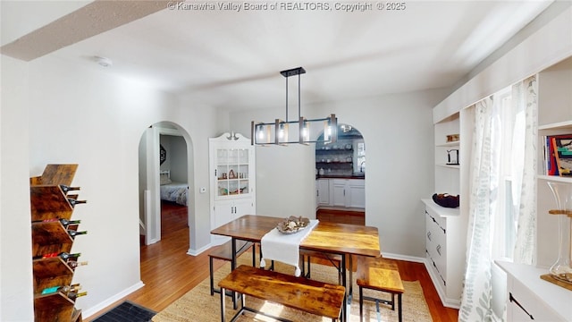 dining area featuring arched walkways, a chandelier, light wood-style flooring, and baseboards