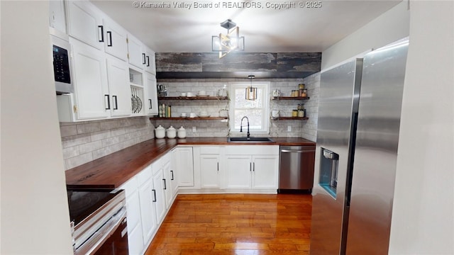 kitchen with a sink, open shelves, stainless steel appliances, light wood finished floors, and wooden counters