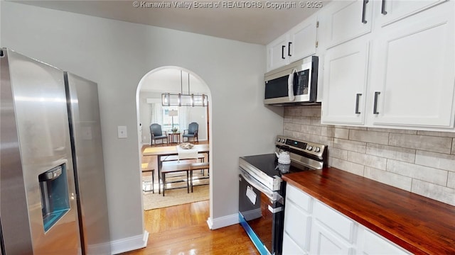 kitchen with light wood finished floors, tasteful backsplash, arched walkways, stainless steel appliances, and wood counters