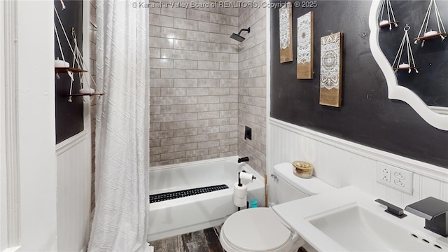 full bathroom featuring wood finished floors, a wainscoted wall, a sink, shower / bath combo with shower curtain, and toilet