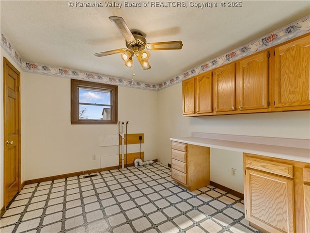 interior space featuring a textured ceiling, built in desk, baseboards, light floors, and ceiling fan