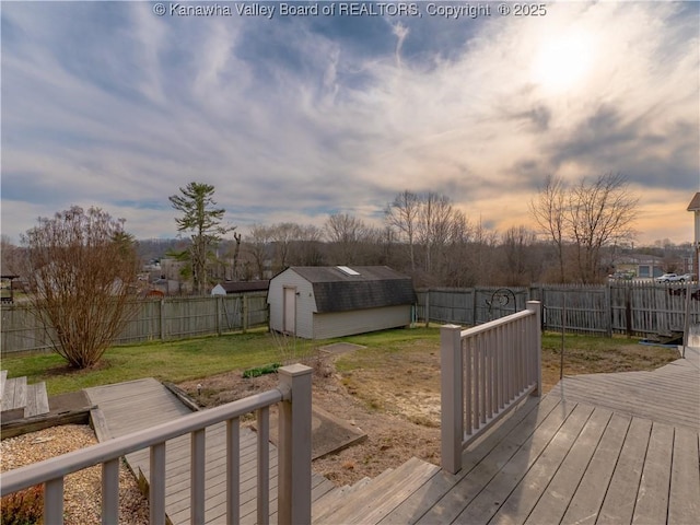 deck at dusk with an outbuilding, a fenced backyard, a lawn, and a shed