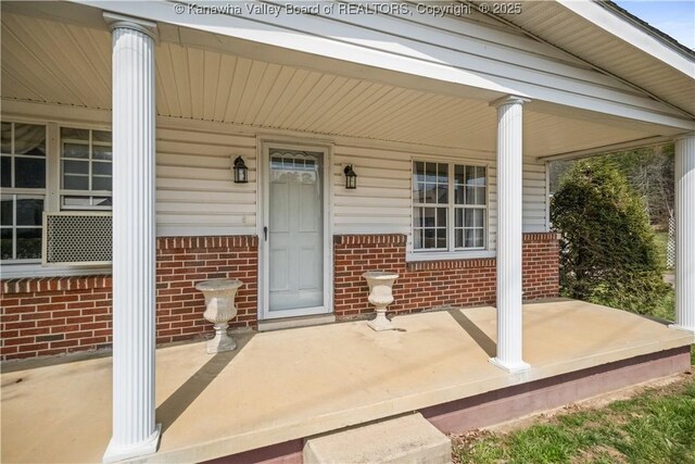 doorway to property with a porch and brick siding