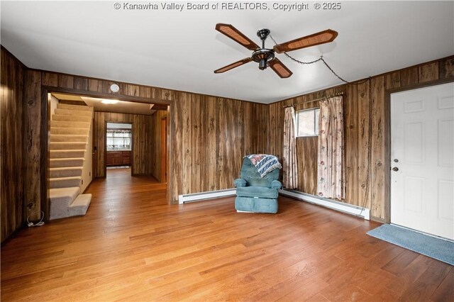 unfurnished room with light wood-style flooring, a ceiling fan, a baseboard heating unit, wooden walls, and baseboard heating