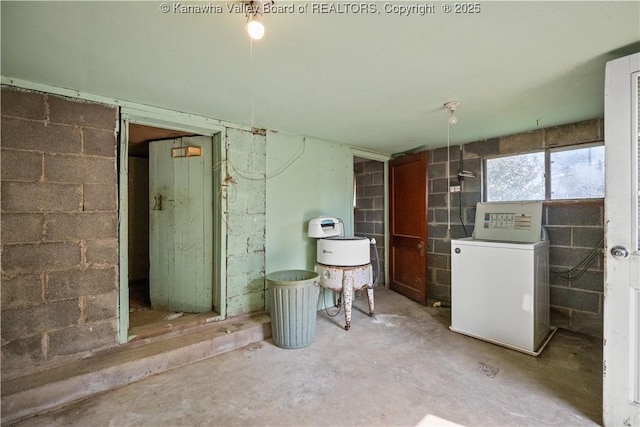 interior space with unfinished concrete floors, washer / clothes dryer, and concrete block wall