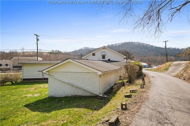 view of side of property featuring a yard, roof with shingles, and a mountain view