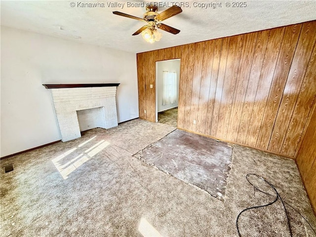 unfurnished living room with wooden walls, a ceiling fan, carpet floors, and a textured ceiling