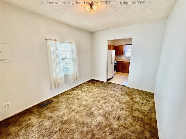 spare room featuring a textured ceiling, baseboards, visible vents, and light carpet