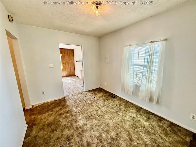 carpeted empty room featuring visible vents, a textured ceiling, and baseboards