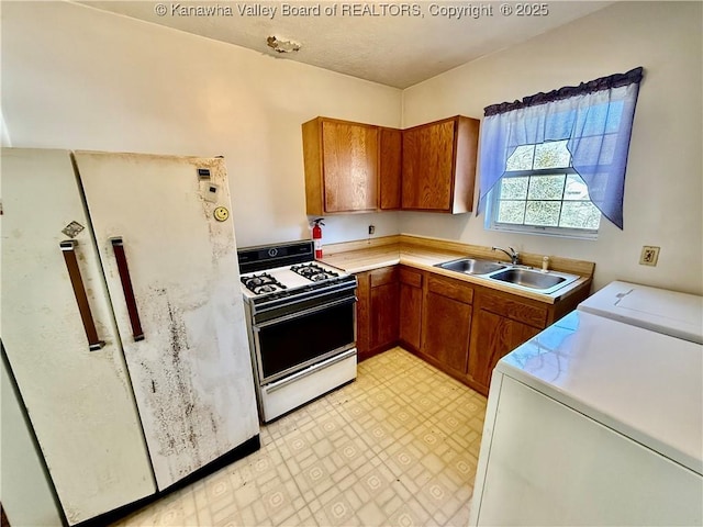 kitchen with brown cabinets, a sink, freestanding refrigerator, range with gas cooktop, and washer / dryer