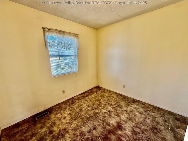 carpeted spare room featuring visible vents, a textured ceiling, and baseboards