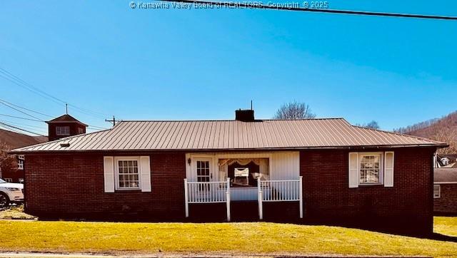 back of house featuring brick siding, a porch, metal roof, a yard, and a standing seam roof