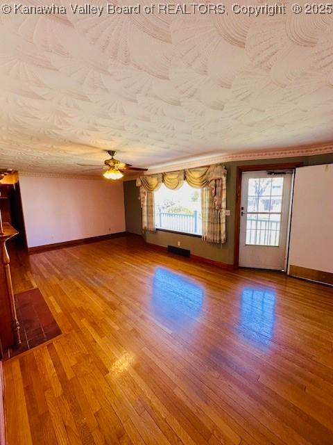 empty room with baseboards, a textured ceiling, wood finished floors, and a ceiling fan