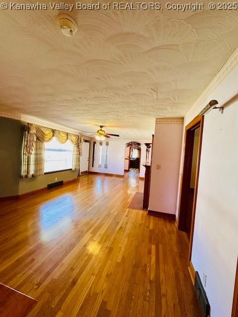 unfurnished living room featuring visible vents, baseboards, ceiling fan, wood finished floors, and a textured ceiling