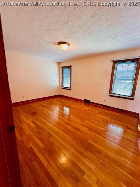 unfurnished room with baseboards, a textured ceiling, and wood finished floors