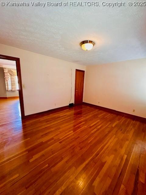 empty room featuring dark wood-style floors, a textured ceiling, and baseboards