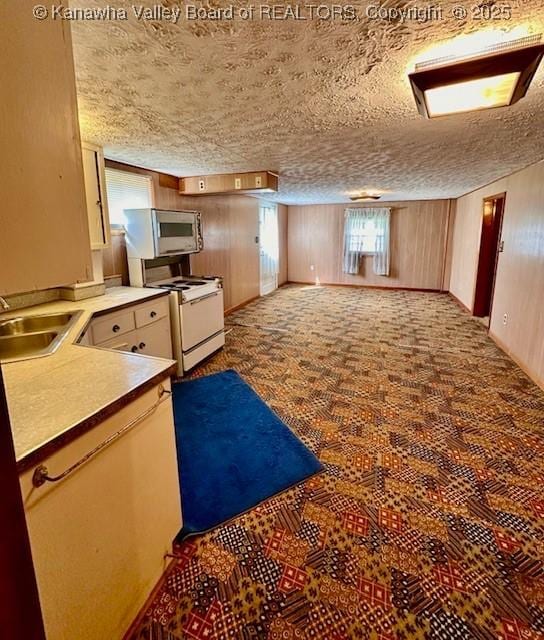 kitchen with a sink, stainless steel microwave, a textured ceiling, wooden walls, and white range with gas stovetop