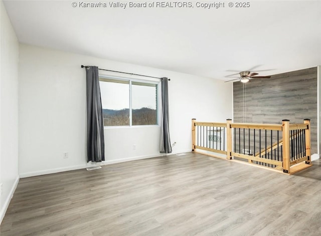 unfurnished room featuring an accent wall, wood finished floors, baseboards, and ceiling fan