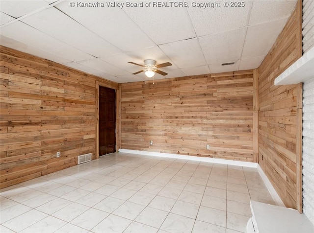 spare room with a paneled ceiling, visible vents, wood walls, and ceiling fan