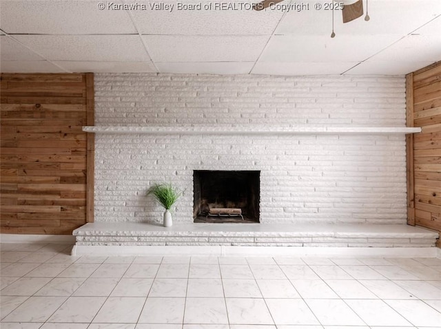 interior details with a drop ceiling, wooden walls, and a brick fireplace