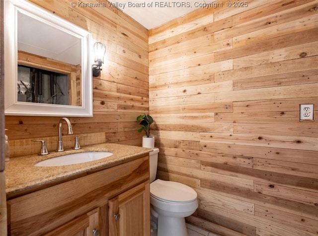 half bathroom featuring wooden walls, toilet, and vanity