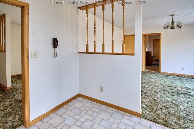 empty room with a notable chandelier, a textured ceiling, and baseboards