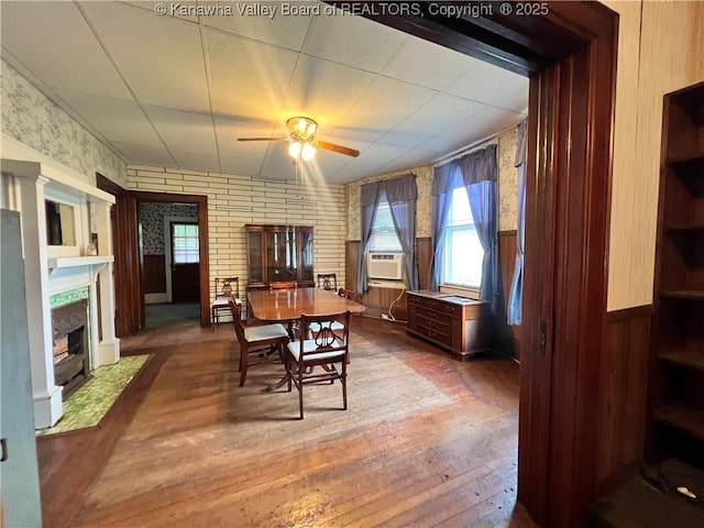 dining room with a healthy amount of sunlight, a wainscoted wall, a fireplace with flush hearth, a ceiling fan, and wood-type flooring