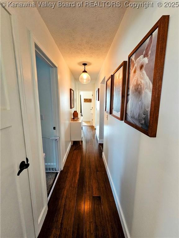 hall featuring a textured ceiling, baseboards, and hardwood / wood-style flooring