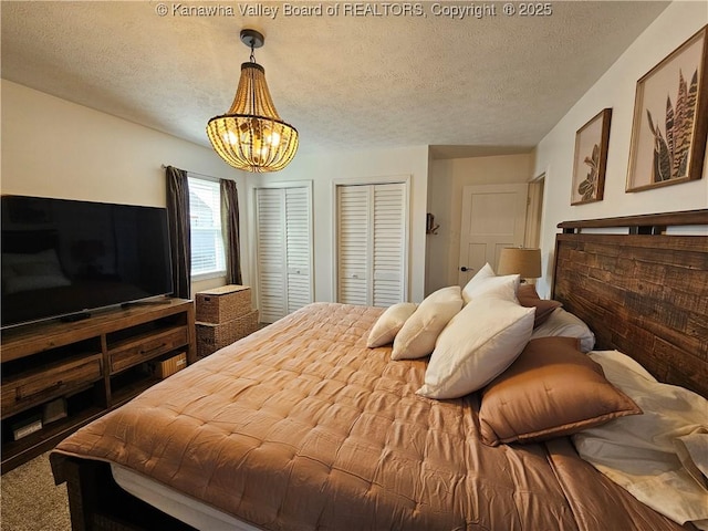 bedroom with carpet flooring, a notable chandelier, multiple closets, and a textured ceiling