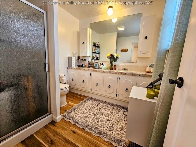 full bath with toilet, a textured ceiling, wood finished floors, a shower stall, and double vanity