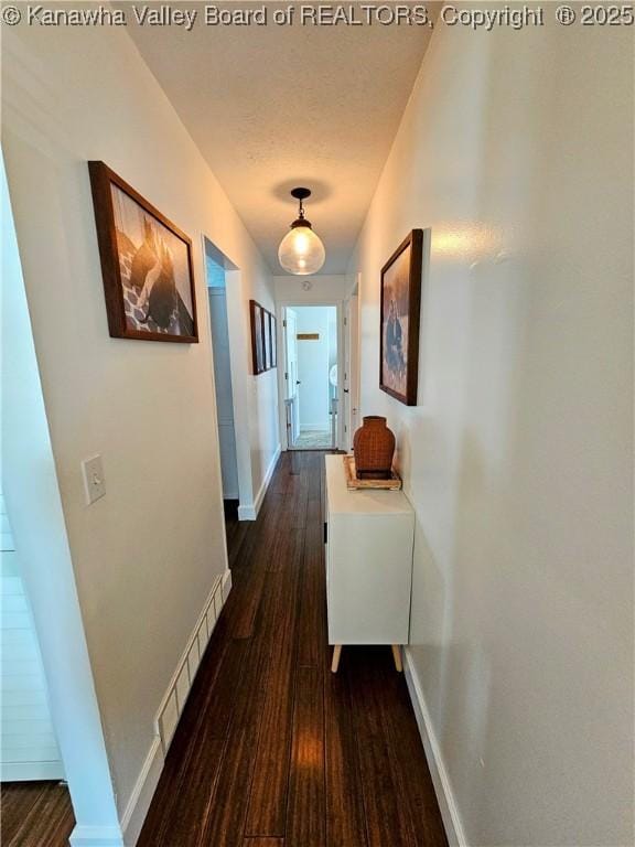 hall featuring dark wood-type flooring, baseboards, visible vents, and a textured ceiling