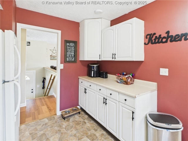 kitchen featuring baseboards, white cabinets, light countertops, and freestanding refrigerator