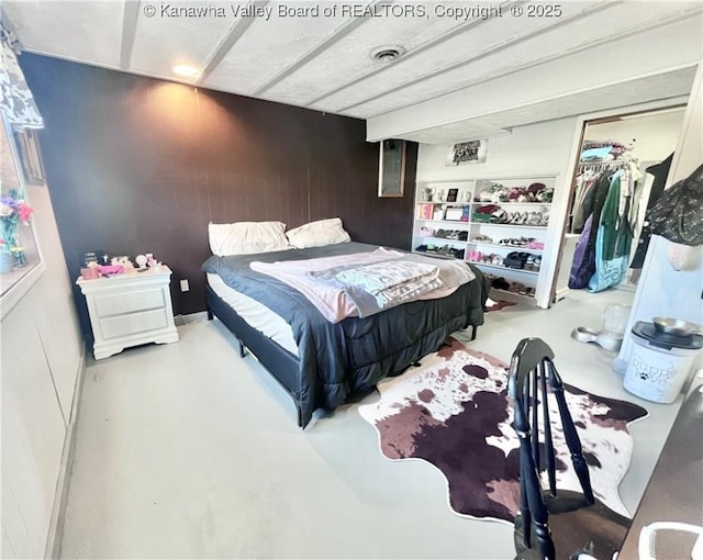 bedroom with a closet, finished concrete flooring, and wood walls