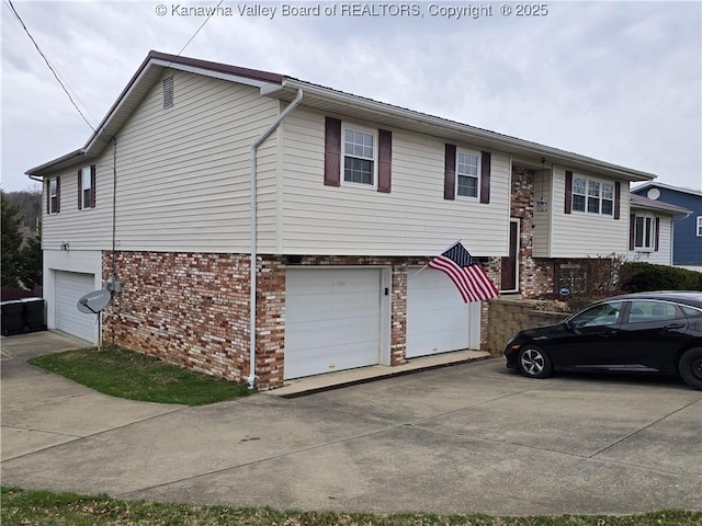 raised ranch featuring brick siding, an attached garage, and driveway