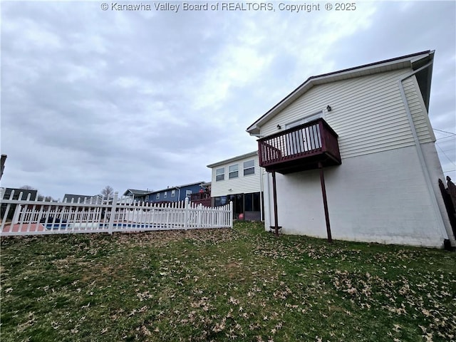 rear view of property featuring concrete block siding, a balcony, a yard, and fence