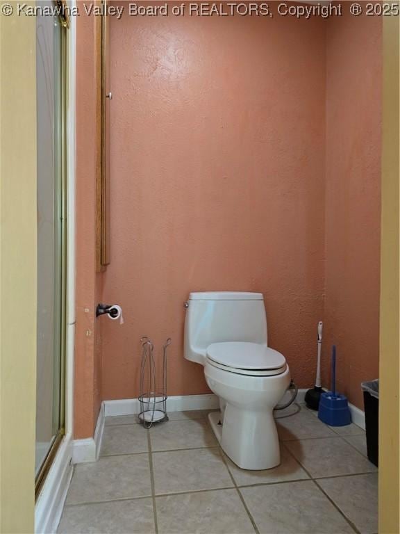 bathroom with tile patterned floors, baseboards, a shower with shower door, and toilet