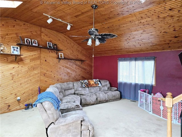 carpeted living room featuring track lighting, wood walls, a ceiling fan, and vaulted ceiling