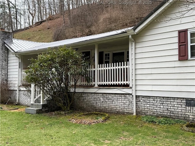 exterior space featuring a porch, a lawn, a chimney, and metal roof
