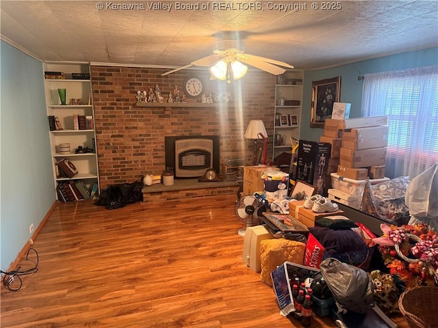 living room with wood finished floors, brick wall, a wood stove, ornamental molding, and ceiling fan