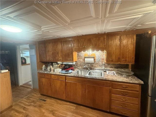 kitchen featuring decorative backsplash, brown cabinetry, an ornate ceiling, and a sink