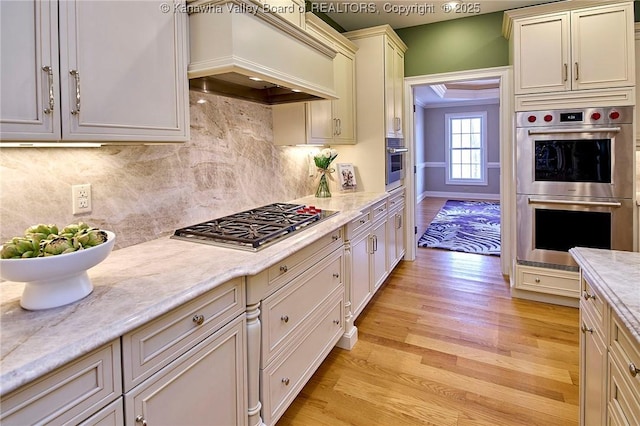 111 Graff Ln, Charleston, WV 25304 - kitchen featuring appliances with stainless steel finishes, custom range hood, light wood-style flooring, light stone counters, and decorative backsplash