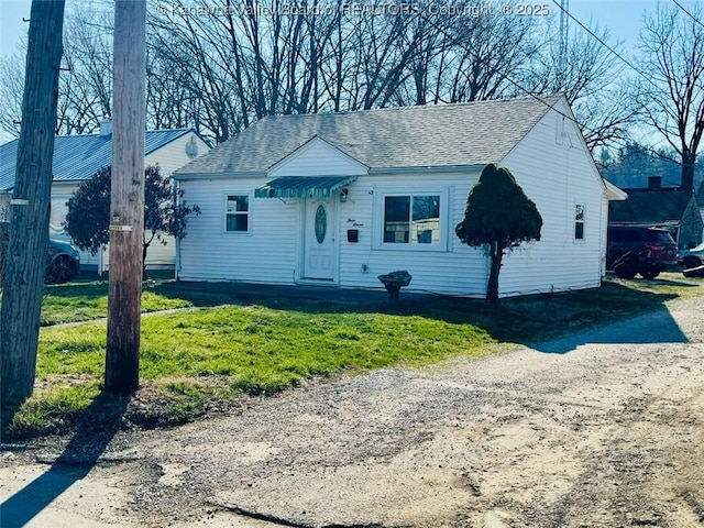 view of front of house with a front yard, dirt driveway, and a shingled roof