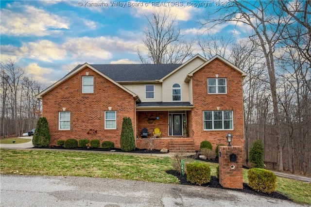 traditional home featuring covered porch, a front yard, and brick siding