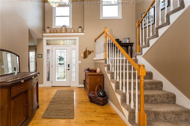 foyer entrance with light wood-style floors, a high ceiling, stairway, and plenty of natural light