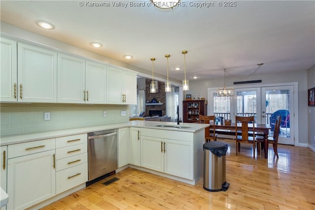 kitchen with decorative backsplash, stainless steel dishwasher, a sink, a peninsula, and light wood-style floors