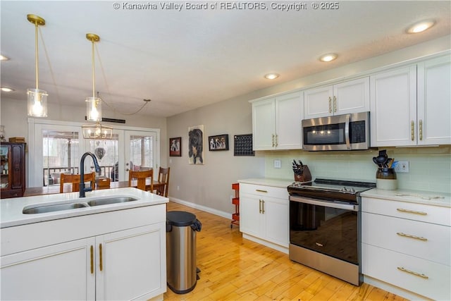 kitchen with backsplash, appliances with stainless steel finishes, a sink, baseboards, and light wood-style flooring