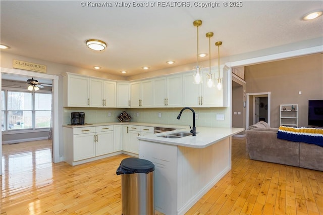 kitchen featuring a peninsula, open floor plan, light countertops, tasteful backsplash, and a sink